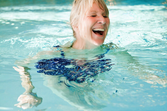 Older woman swimming in an indoor pool and doing water gymnastics.