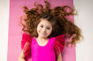 Tired little girl lying down after gym training on a yoga mat with long blonde hair scattered.