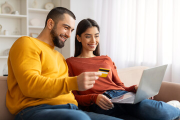 Online Shopping. Happy Couple With Laptop And Credit Card Relaxing At Home