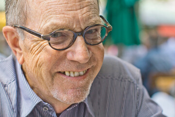 Older senior gentleman with glasses smiling in the camera. Munich, Germany