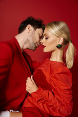 pretty woman in dress and red earrings seducing handsome man on red background, fashionable couple