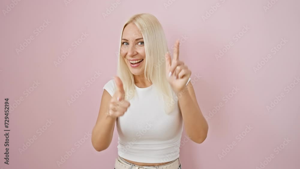 Sticker Cheerful young blonde woman caught in good vibes, posing and pointing at you over isolated pink background, positive energy and funny happiness!