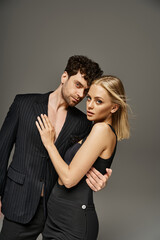 beautiful man and woman in evening attire posing together on grey background, charming couple