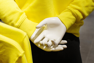 Hands of a plastic mannequin in a bright yellow sweater on a clothing store window close-up