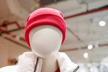 Close-up portrait of a faceless mannequin in a red hat and white jacket on a clothing store window, soft focus.