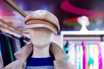 Close-up portrait of a faceless mannequin in a brown leather cap and coat in a clothing store window, soft focus.
