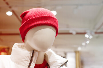 Close-up portrait of a faceless mannequin in a red hat and white jacket on a clothing store window, soft focus.