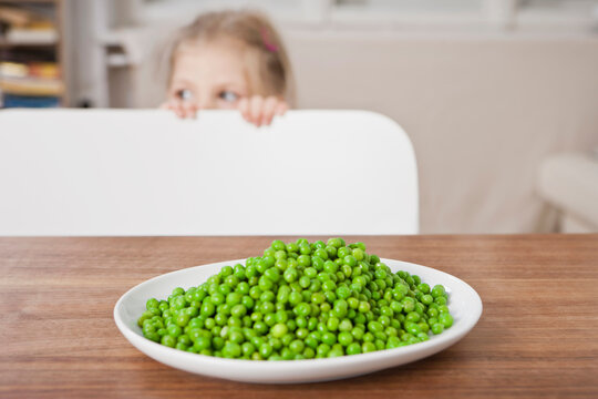 Still life of plate full of peas and child looking over chair.