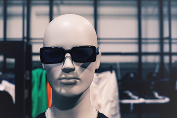 Faceless mannequin in black sunglasses on the showcase of a clothing store close-up, soft focus.	