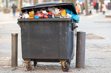 Überquellender Müllcontainer, der auf der Straße steht und auf seine Abholung durch die...