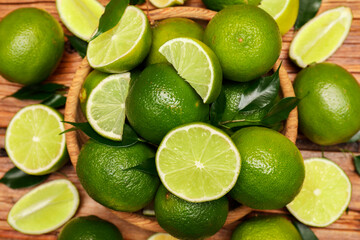 Fresh limes and green leaves on wooden table, top view