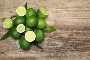 Pile of fresh limes and green leaves on wooden table, flat lay. Space for text