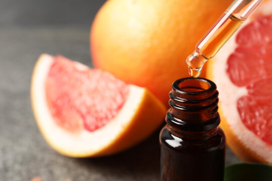 Dripping grapefruit essential oil from pipette into bottle and fresh fruit on table, closeup. Space for text