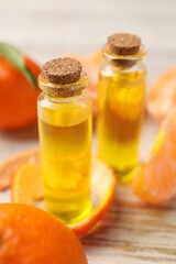 Bottles of tangerine essential oil, fresh fruits and peel on white wooden table, closeup