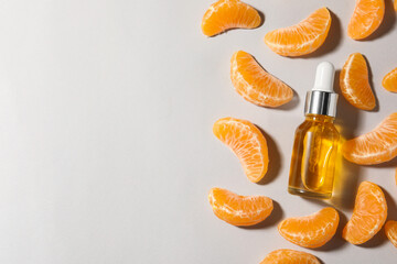 Aromatic tangerine essential oil in bottle and citrus fruit on grey table, flat lay. Space for text
