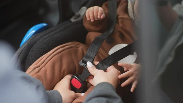 Close-up cropped shot of unrecognizable young mother fastening safety belt to infant baby boy in car seat. Cute toddler with security belt in vehicle. Concept of safety lifestyle, driving and travel.