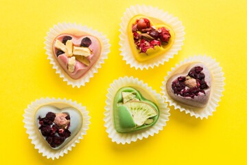 chocolate sweets in the form of a heart with fruits and nuts on a colored background. top view with space for text, holiday concept