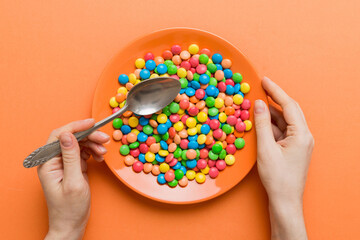 the girl holds cutlery in her hands and eats sweets in a plate. Health and obesity concept, top view on colored background