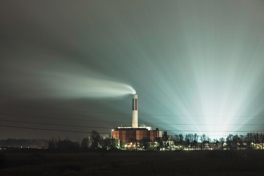 Nightscape landscape of cooling tower from a factory with fog and light installation behind. Bremerhaven, Germany