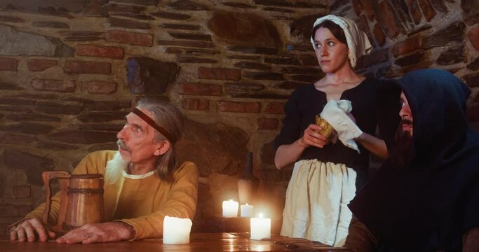 Man keeps eyes on new guest while disinterested maid cleans mug in pub. Constant visitors and sarcastic servant prepare for troubles from newbie in medieval pub