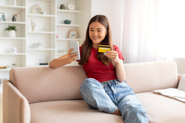 Delighted asian woman engaging in online shopping with smartphone and credit card