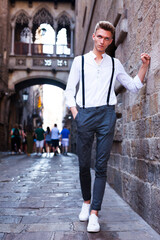 Young European guy in shirt and trousers with suspenders walking around city