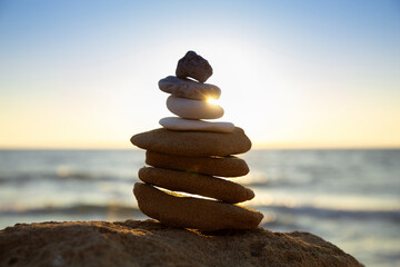 Stones placed one on one, balancing on the beach, shot against the backdrop of sunrise or sunset. Zen meditation and relaxation on the beach