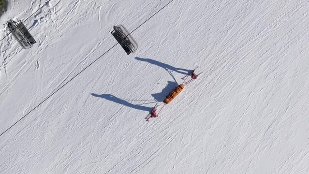 Saving a skier from a mountain winter ski slope accident. 4K aerial view of an emergency mountain rescue team getting down on a rescue sledge.