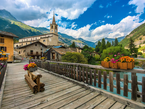 Wooden bridge over alpine river and houses with church in Val-Cenis, France.
