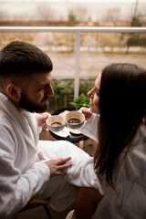 Morning gaze. Lovers in bathrobes share hotel breakfast, eyes locked.