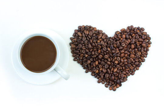 A pile of coffee beans in the shape of a heart, a cup of coffee on a white background. Top view.