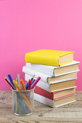 Books stacking. Books on wooden table and pink background. Back to school. Copy space for ad text.