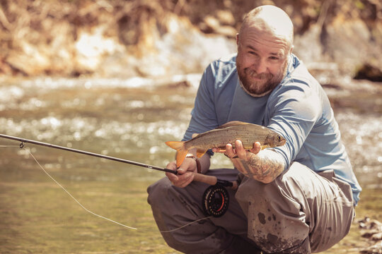 Fly fisherman presenting his small fish he caught in a river. Mozirje, Slovenia