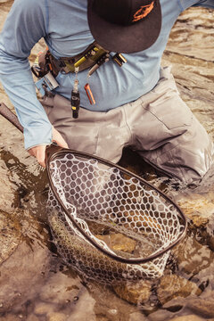 Fly fisherman walking through river with caught fish in his net. Mozirje, Slovenia