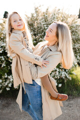 Fototapeta premium Happy young mother holding child girl 4-5 year old wearing beige similar jacket in sun light outdoor. Motherhood. Spring season.