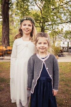 Young girl wearing a white spring dress and a flower wreath in her hair next to her sister. Munich, Germany
