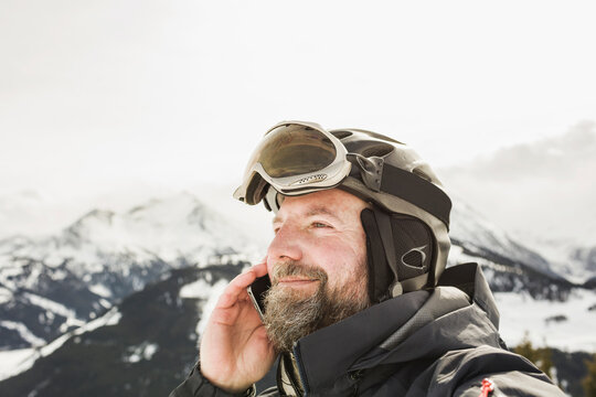 Portrait of happy man while up on ski slope, wearing helmet and goggles, talking on his cell phone.. Zillertal, Austria