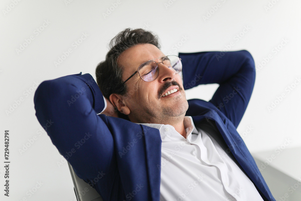 Wall mural Relaxed businessman in a blue suit reclining in his chair with his hands behind his head