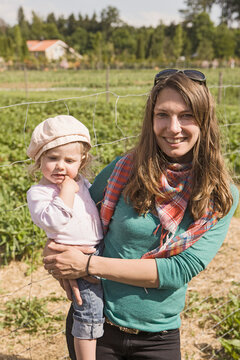 Mother holding her young daughter while standing in a strawberry field. Strasslach, Germany