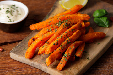Sweet potato sticks served with white sauce on a cutting board, top view. Vegetarian food and...