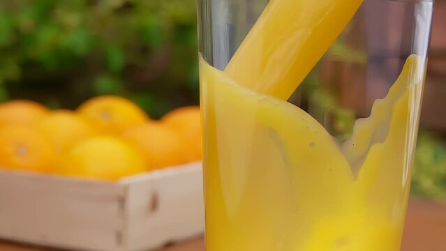 Delicious orange juice swirls into a wave in a glass against the background of cut oranges.