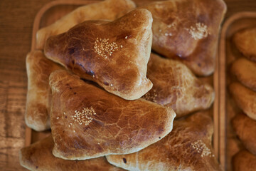 Fresh baked goods: samsa with meat, sprinkled white sesame seeds lies in heap on wooden plate. Puff pastry samosa top view. Asian food, Traditional eastern cuisine Tajikistan, Uzbekistan, Kyrgyzstan
