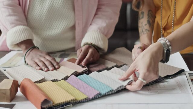 Cropped shot of two unrecognizable diverse male and female designers choosing house finishing color using sample palette while working on project together in creative workshop