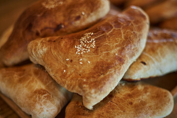 Fresh baked goods: samsa with meat, sprinkled white sesame seeds lies in heap on wooden plate....