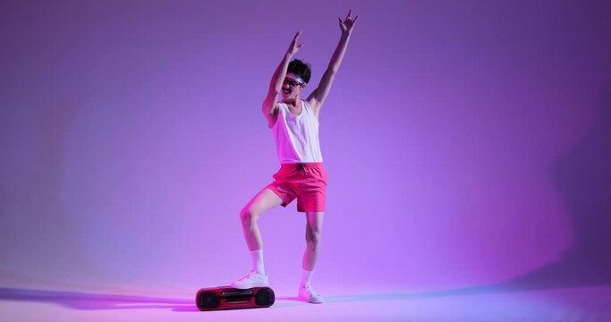Funny nerdy young Caucasian 80s man dancing on discotheque using ghettoblaster for playing music, standing over purple background.