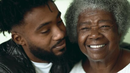 Adult grandson kissing elderly African American grandmother on the cheek in tender affectionate loving moment between two intergenerational family members