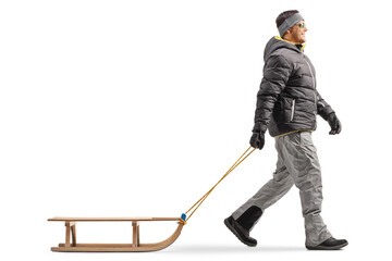Full length profile shot of a man in a winter jacket walking and pulling a wooden sled