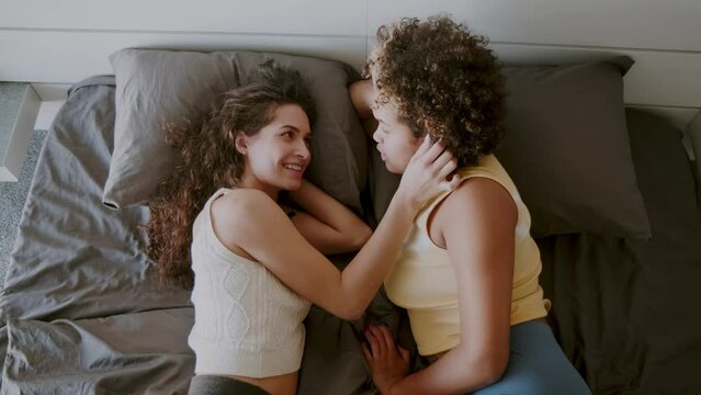 From above view shot footage of young women spending morning together relaxing on bed, touching each other and talking about something