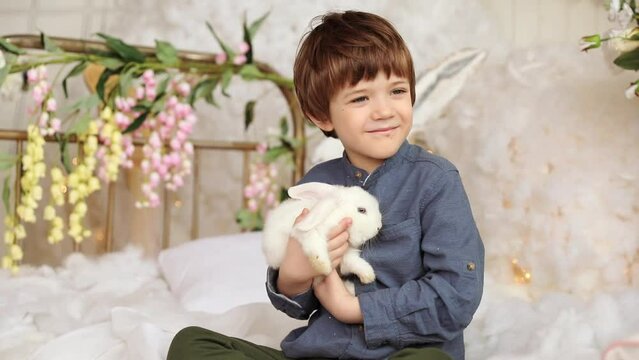 White Easter rabbit sits on the hands of a little boy, who huggs the rabbit