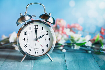 Set your clocks forward with this clock and flowers over a rustic teal wooden table. Daylight saving time concept. Selective focus with blurred background.